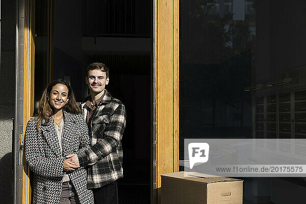 Portrait of smiling multiracial couple holding hands while standing in front of apartment