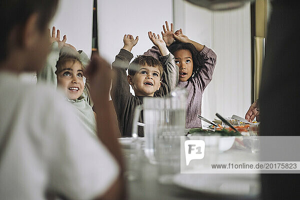 Happy children with arms raised during lunch time at kindergarten