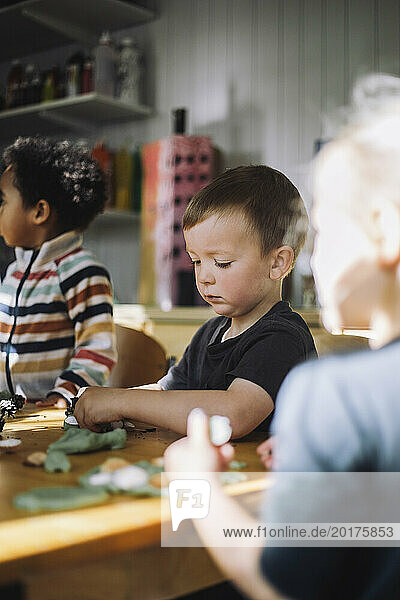 Schoolboy playing with clay while sitting at bench during art class at kindergarten