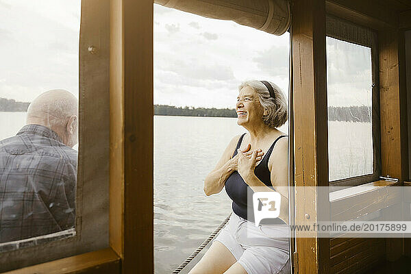 Happy senior woman with hands on chest sitting near man at houseboat