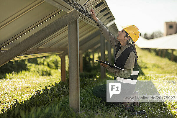 Side view of female engineer examining solar panels while kneeling at power station