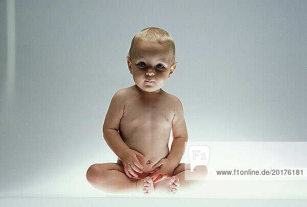 Studio image of naked baby sitting upright.