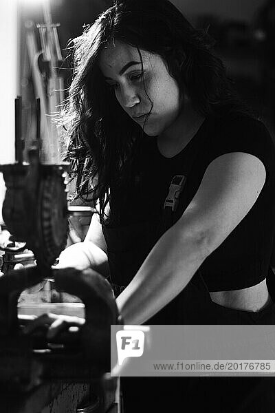 Hispanic latino langhaarige brunette sexy Frau Mechaniker Prüfung eines Autoteil in einer gut ausgestatteten Werkstatt  eine komplette Werkzeugplatte in der unscharfen Hintergrund mit Bokeh Effekt