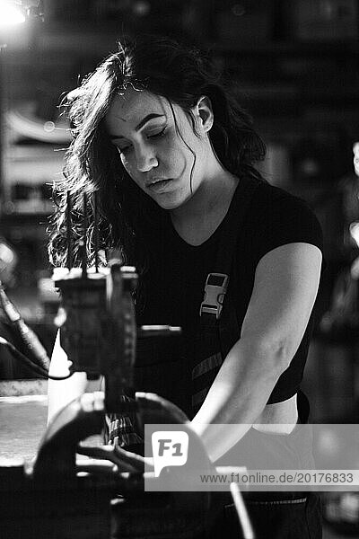 Hispanic latino langhaarige brunette sexy Frau Mechaniker Prüfung eines Autoteil in einer gut ausgestatteten Werkstatt  eine komplette Werkzeugplatte in der unscharfen Hintergrund mit Bokeh Effekt