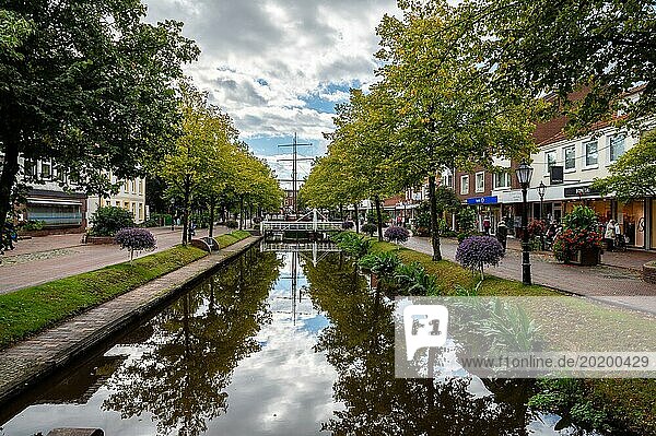Ein ruhiger Kanal fließt durch eine Stadt  gesäumt von Geschäften und Blumen unter einem bewölkten Himmel  Papenburg  Emsland  Niedersachsen