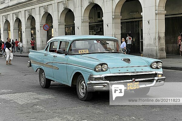 Hellblauer Oldtimer als Taxi auf einer belebten Straße mit Passanten im Hintergrund  Havanna  Kuba  Mittelamerika