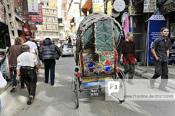 Eine bunt geschmückte Rikscha fährt auf einer belebten Straße mit Fußgängern  Impressionen von Nepal  Fahrt von Pokhara-Tal nach Kathmandu Nepal