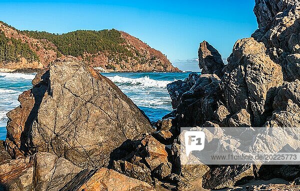 Foamy waves hitting the rocky shores of a vibrant blue sea on a sunny day with a clear sky  in South Korea
