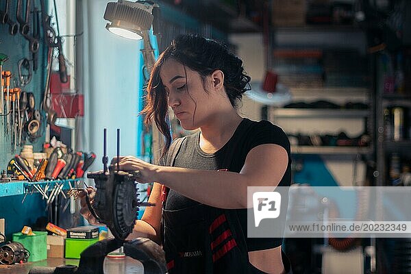 Eine Handwerkerin ist sorgfältig mit Reparaturarbeiten beschäftigt  umgeben von Werkzeugen in ihrem Beruf  eine komplette Werkzeugtafel im Hintergrund mit Bokeh Effekt  traditionelle Männerberufe von Mixed race latino woman