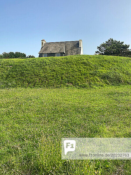 Ein kleines Haus steht hinter dem Hügel auf einer gruenen Wiese. Frankreich  Bretagne  Quiberon
