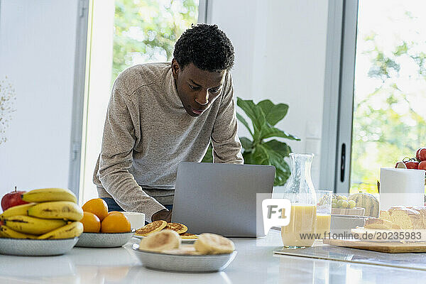 Adult man using laptop while standing at kitchen counter