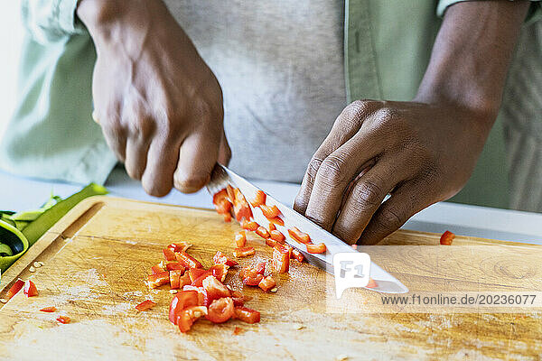 Close up of man's hands cutting vegetable with sharp knife on cutting board