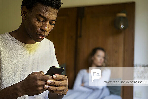 Adult man using smart phone while girlfriend is lying with crossed arms on the background