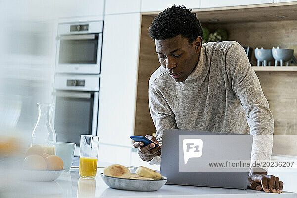 Adult man using smart phone while standing at kitchen counter