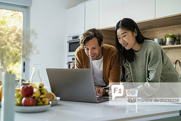 Adult couple shopping online on laptop and smart phone at kitchen counter