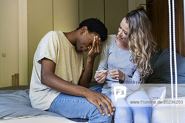 Disappointed man with hand on face sitting next to girlfriend with pregnancy test