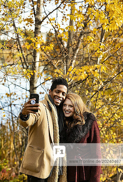 Close-up of a mixed race married couple taking a selfie together while spending quality time together during a fall family outing in a city park; Edmonton  Alberta  Canada