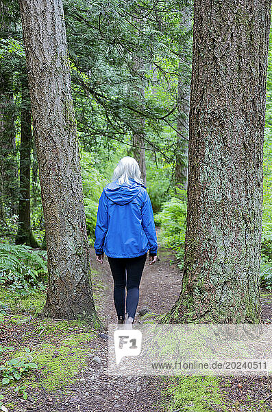 View taken from behind of a woman walking along a dirt path through Watershed Forest Trail; Delta  British Columbia  Canada