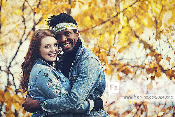 Close-up portrait of a mixed race married couple embracing and smiling at the camera  spending quality time together during a fall family outing in a city park; Edmonton  Alberta  Canada