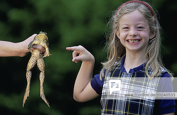 Young girl points to a frog being held by someone off camera; Lincoln  Nebraska  United States of America