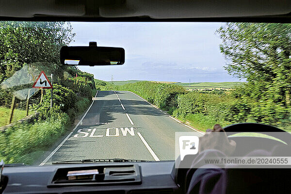 View from a car of a road marked with the word 'slow' and the surrounding English countryside; Great Britain