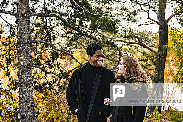 A mixed race couple smiling at each other walking through the woods  spending quality time together during a fall family outing in a city park; Edmonton  Alberta  Canada