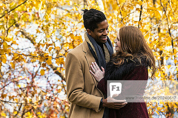 Close-up portrait of a mixed race couple hugging and smiling at each other while spending quality time together during a fall family outing in a city park; Edmonton  Alberta  Canada