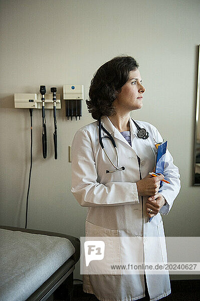 Physician's assistant holds a clipboard while looking out the window of an empty patient room; Lincoln  Nebraska  United States of America