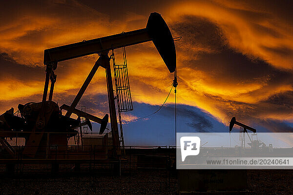 Silhouette of pumpjacks against a colourful dramatic sun set sky with warm glowing clouds  West of Airdrie; Alberta  Canada