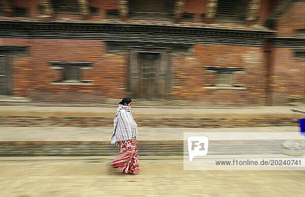 Panned view of a Nepalese woman hurrying past a brick building; Kathmandu  Nepal