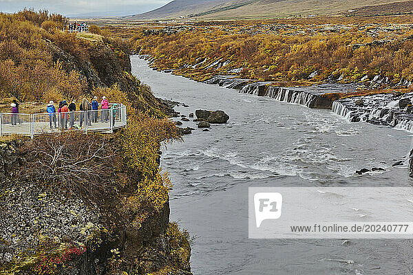 Tourists stand at a lookout point with a view of Hraunfossar falls near Reykholt in Western Iceland; Iceland