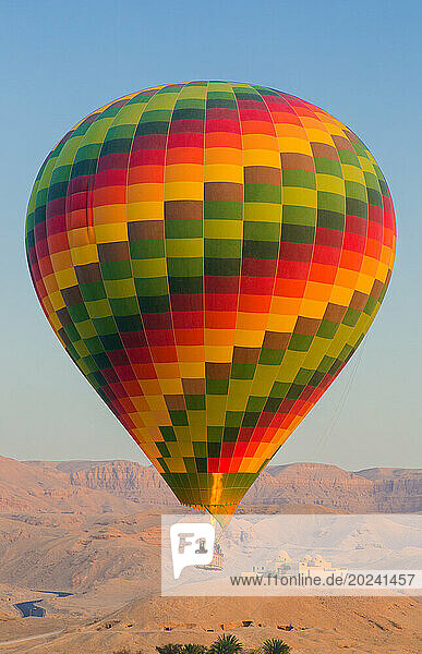 Hot air balloon carrying tourists over the Vally of the Kings and Howard Carters home on the ridge; Luxor  Egypt