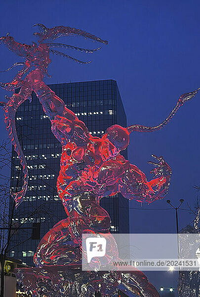 Ice sculpture of warrior in red light  with buildings and lights in the background
