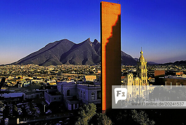 View of the State Capital City of Monterrey  with the natural monument of the saddle-back mountain of Cerro de la Silla contrasted against the orange  modern  monolithic tower of Faro Del Comercio (Beacon of Commerce) and the Baroque style  historical Cathedral of Monterrey in Macroplaza of the city center; Monterrey  Nuevo León  Mexico