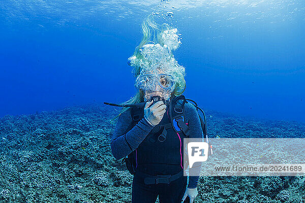 Diver pictured with big eyes and bubbles looking uncomfortable underwater over a hard coral reef off the island of Maui  Hawaii  USA; Maui  Hawaii  United States of America
