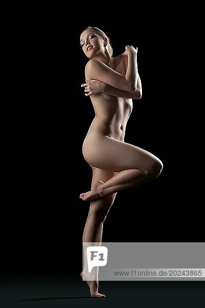 Ganzes Porträt einer nackten jungen Frau  die in einem dunklen Studio posiert