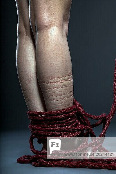 Mit rotem Seil gefesselte Beine einer schlanken Frau  Nahaufnahme