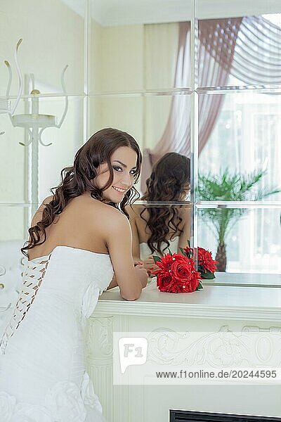 Attraktive lächelnde lockige Braut posiert vor einem Spiegel