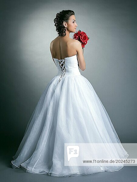 Bild von jungen schlanken Modell posiert in Hochzeitskleid  auf grauem Hintergrund