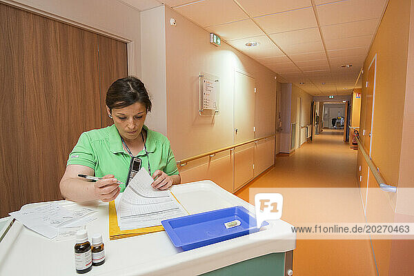 EHPAD - Nurse with her trolley in an empty hallway consulting a resident's file.