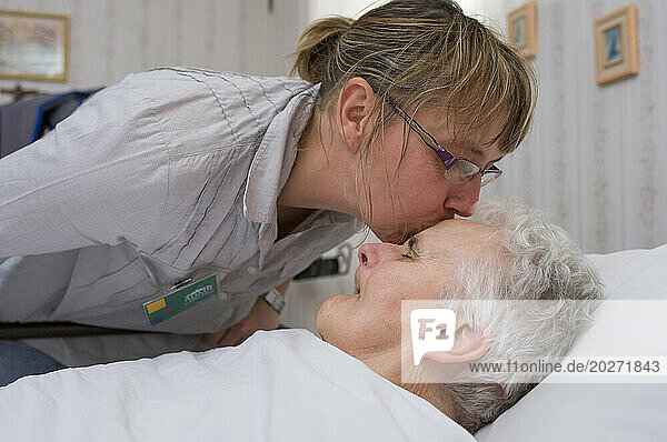 ADMR 62 - Home Help in Rural Areas  Pas de Calais. Veronique  Auxiliary of Social Life (AVS) intervenes in the home of Mr. and Mrs. B.  severely handicapped by Alzheimer's disease. Veronique must help him with all the daily tasks. Caregiver kissing a bedridden dependent elderly person before leaving the room.