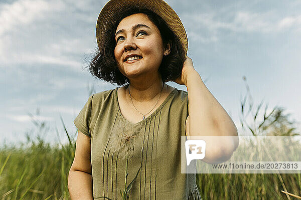 Smiling mature woman wearing hat and holding dandelion in field