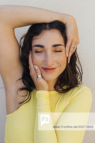 Smiling woman with eyes closed against white background touching her face