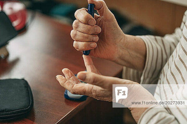 Senior woman pricking finger to measure blood sugar level at home