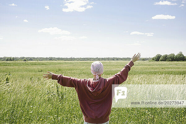 Carefree boy standing with arms outstretched in field on sunny day