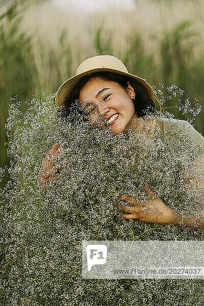 Smiling woman embracing bunch of gypsophila flowers in field