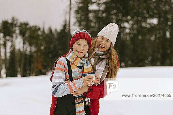 Happy mother and son wearing warm clothes in winter forest