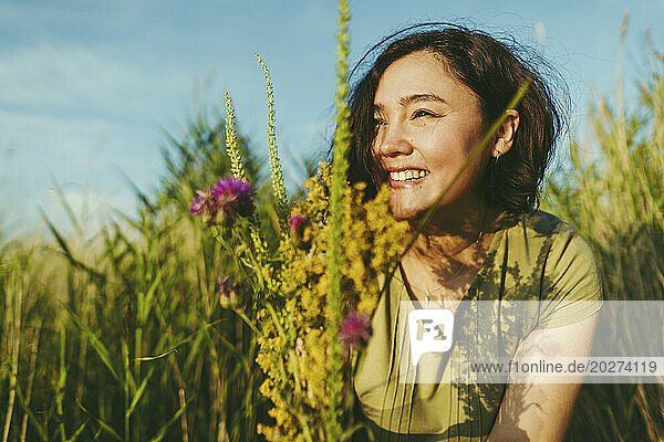 Happy woman with bunch of wildflowers in field on sunny day