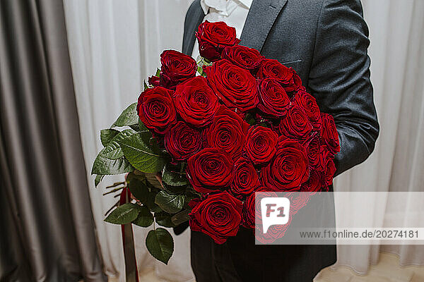 Teenage boy holding bouquet of red roses at home