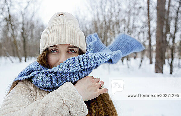 Young woman wearing knit hat and blue scarf in winter forest